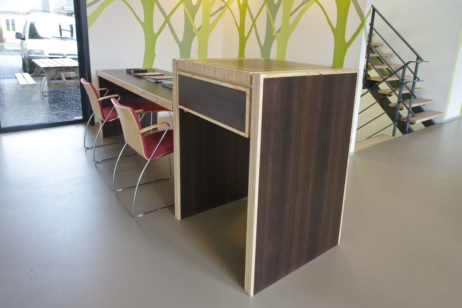 Balie met een donker front, een lichte houten rand en een lade, met stoelen ervoor.
