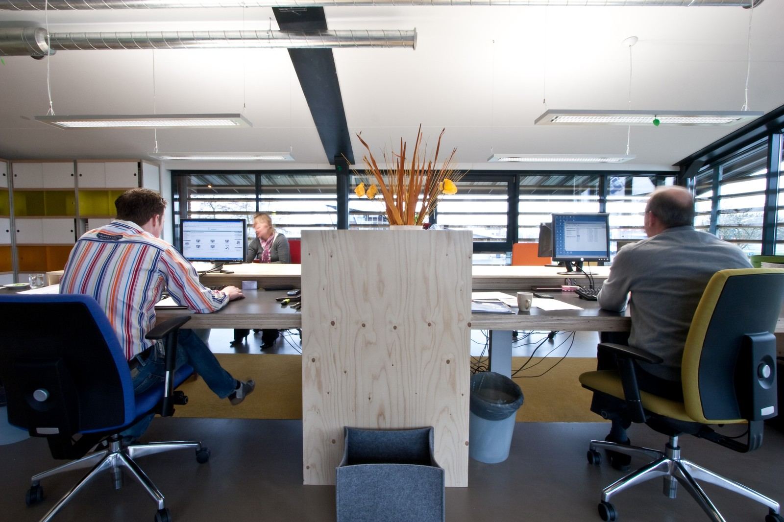 Vuren multiplex scheidingswand tussen twee werkplekken, met opbergvak onderaan.