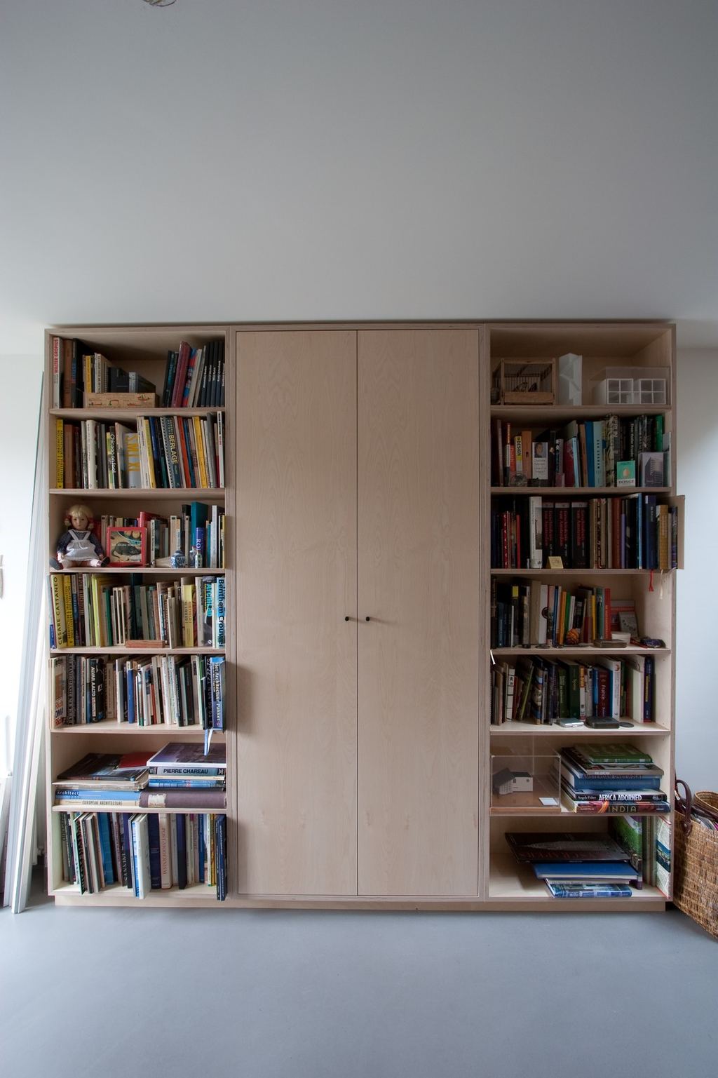 Boekenkast met een middenkast met deuren, geflankeerd door open planken vol boeken.