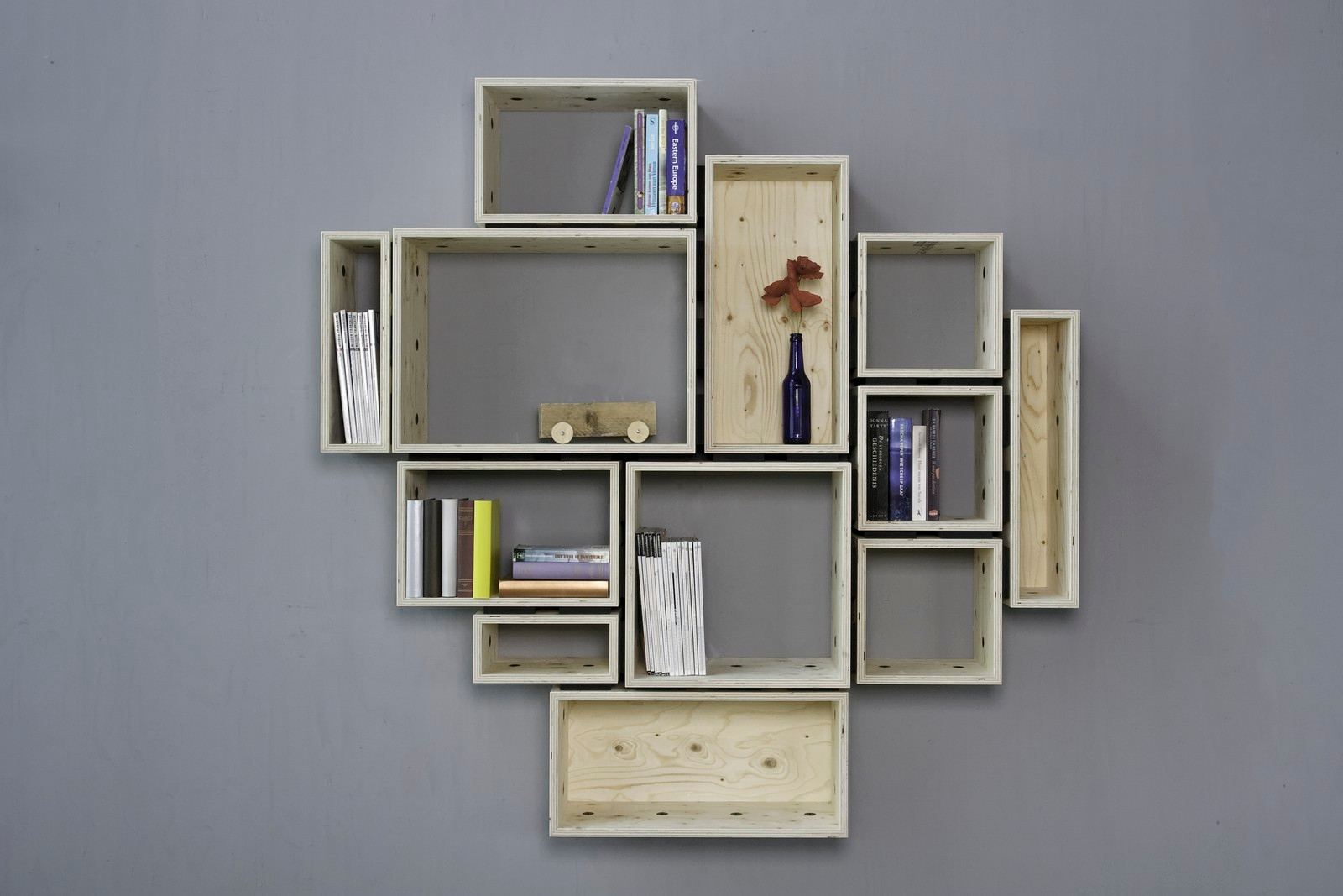 Cluster van lichte kastvakken in multiplex met boeken en een speelgoedautootje.