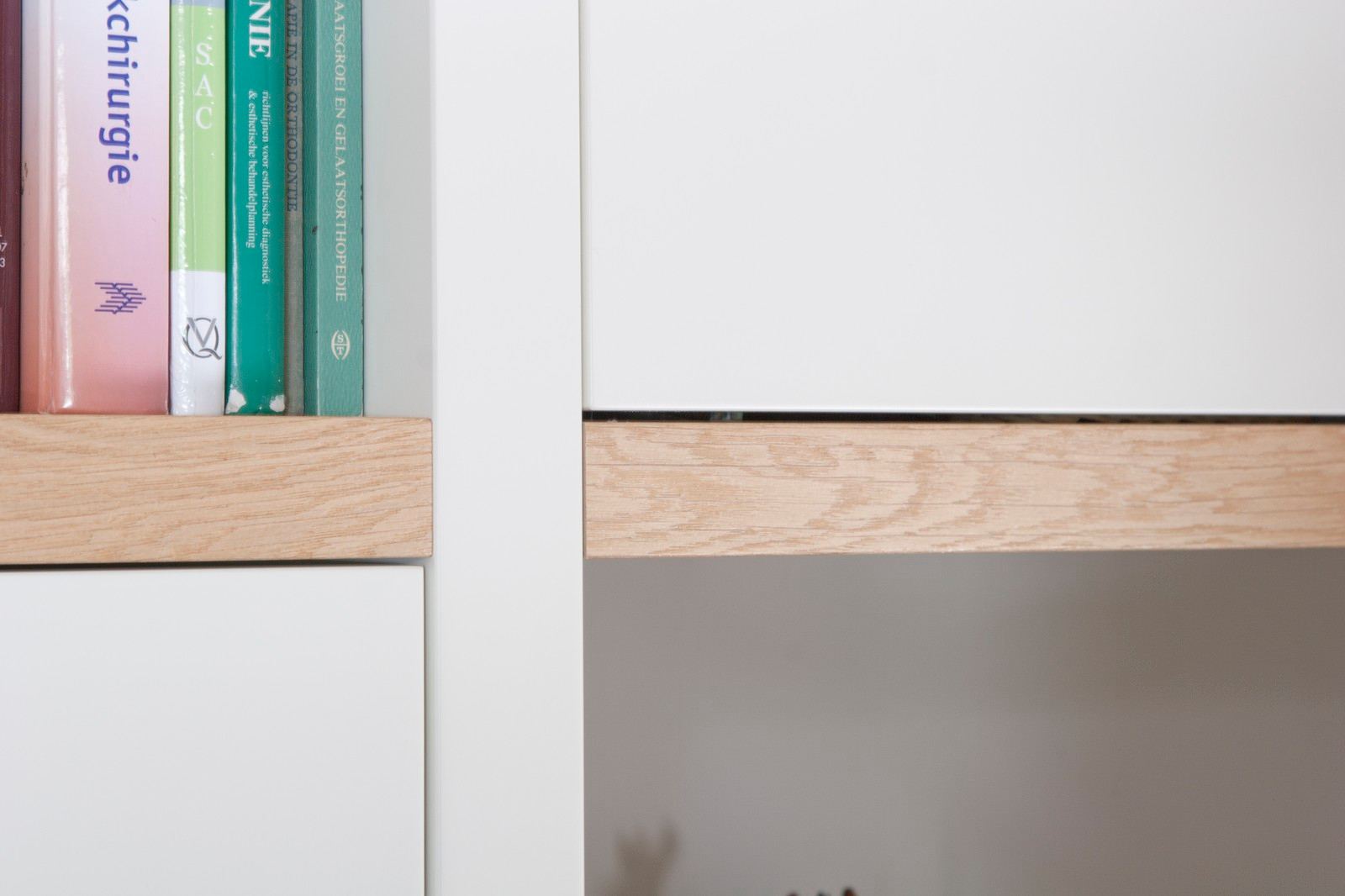 Detail van een eiken plank tussen twee witte kastdeuren.