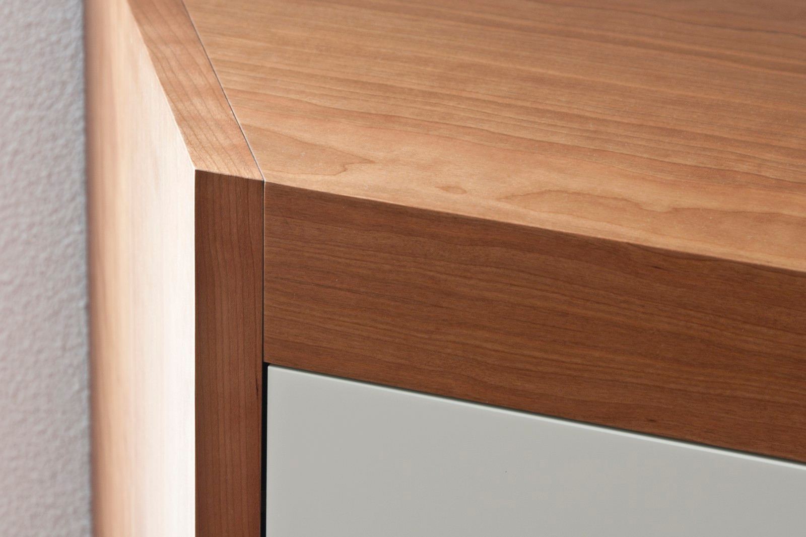 Detail van de kersen fineer hoekverbinding boven een witte kastdeur.