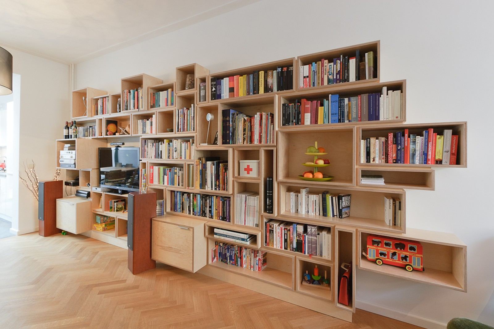Wandvullende boekenkast van berken multiplex met een onregelmatig rooster van vakken.
