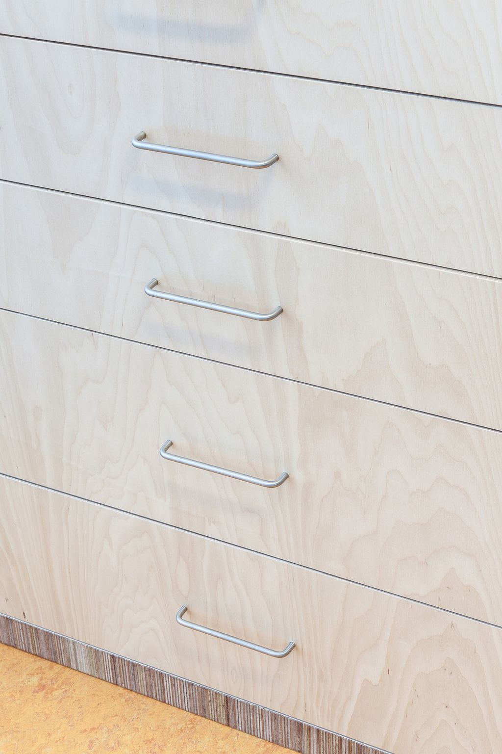 Detail van een ladenkast in berken multiplex met metalen grepen.