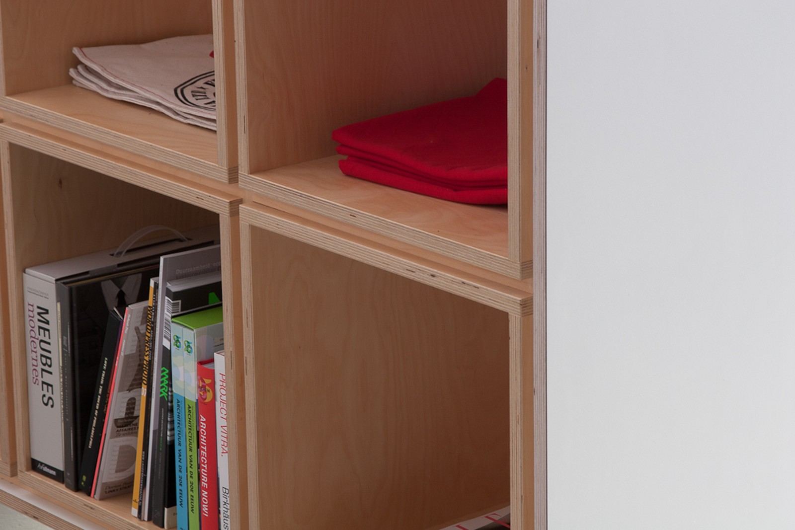 Detail van vakken met opgevouwen doeken en boeken naast een wit zijpaneel.