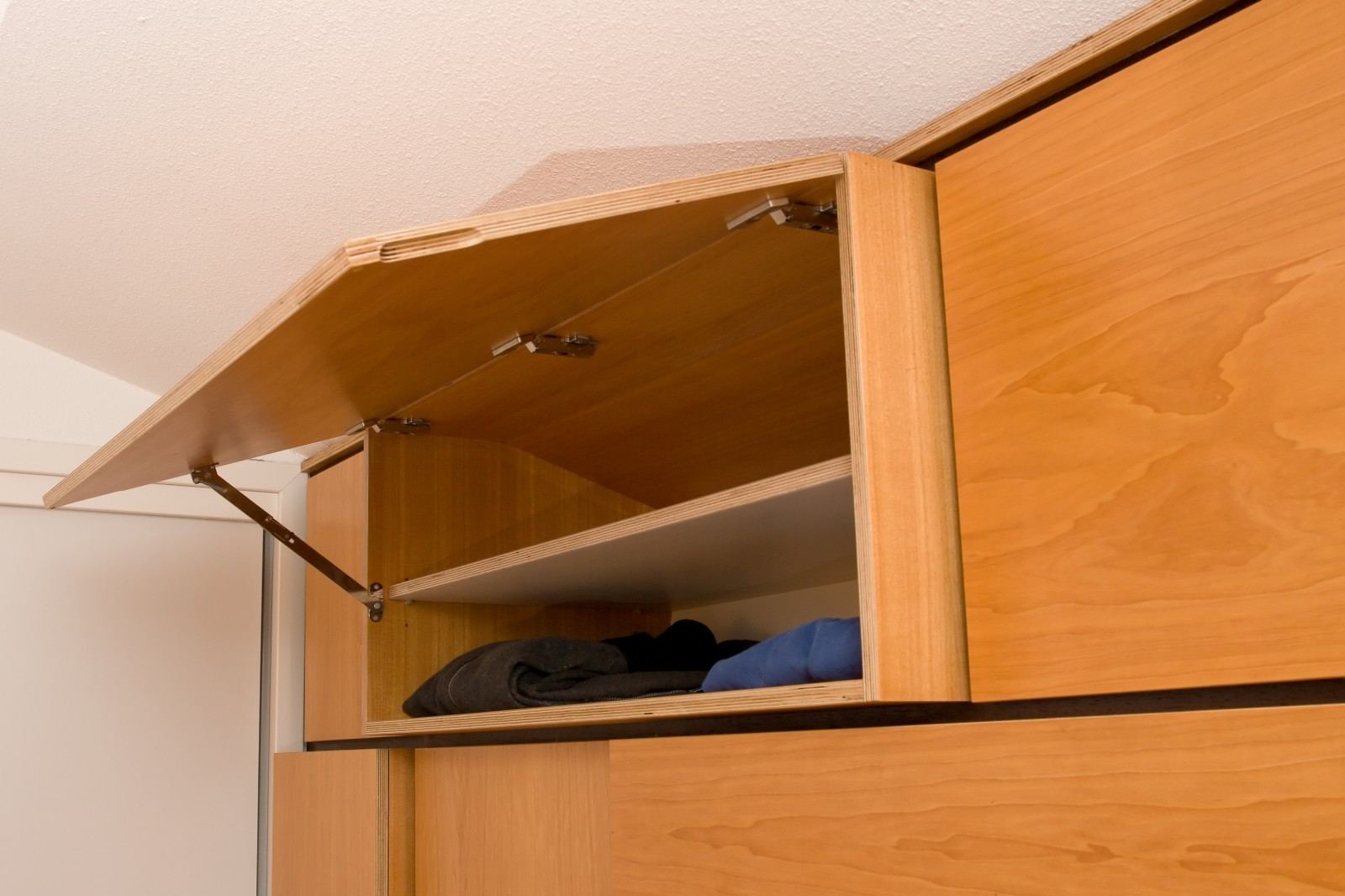 Open klepdeur van de garderobekast met berken multiplex binnenkant en kleding.