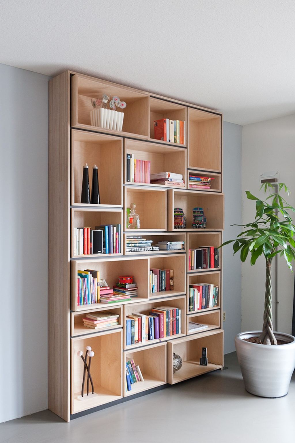 Puzzelvormige boekenkast van losse vakken in verschillende maten, gevuld met boeken en kleine objecten.