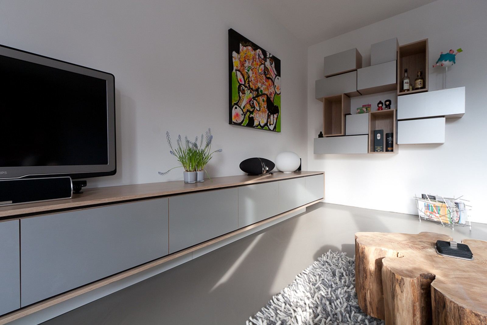 Zwevend tv-dressoir en een cluster losse kastjes aan de wand.
