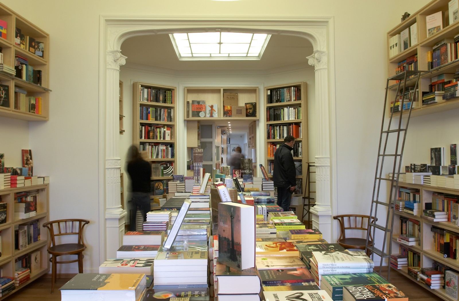 Open boekenkasten van berken multiplex met een verrijdbare ladder ervoor.