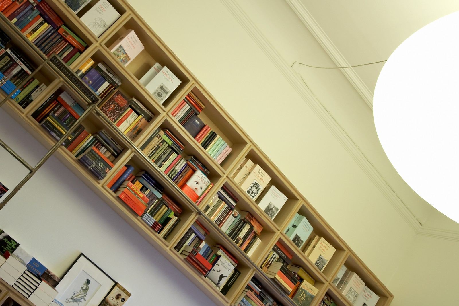 Wandvullende boekenkast van berken multiplex die schuin oploopt met de zoldering.