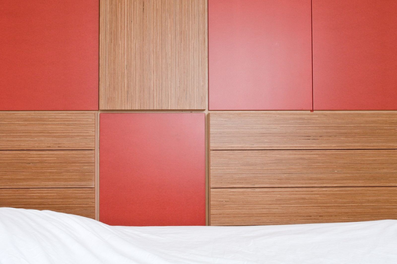 Garderobekast met rode en gestreepte plexwood vakken boven het bed.