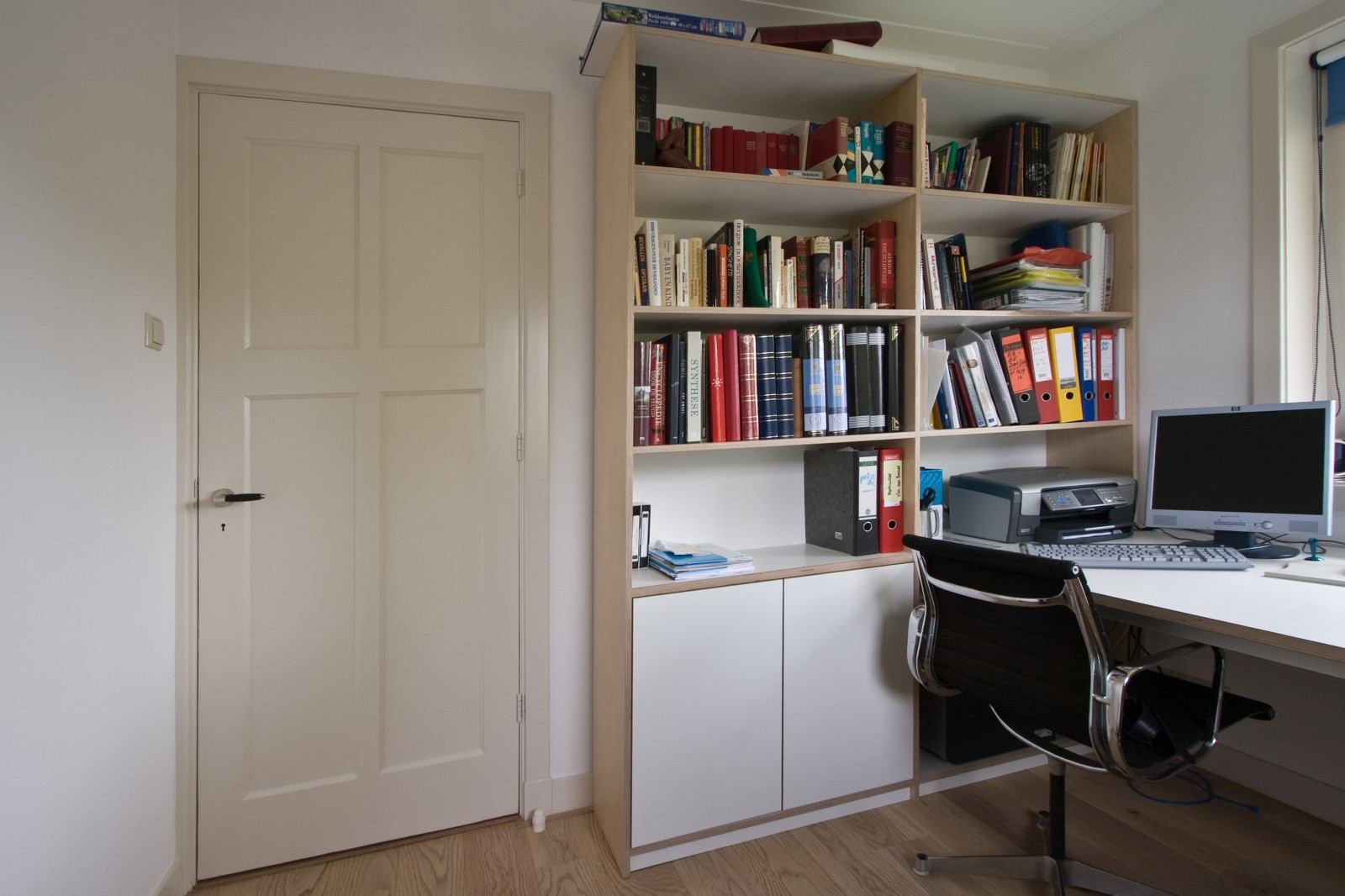 Boekenkast met witte kastdeuren en een geïntegreerd bureau ernaast.