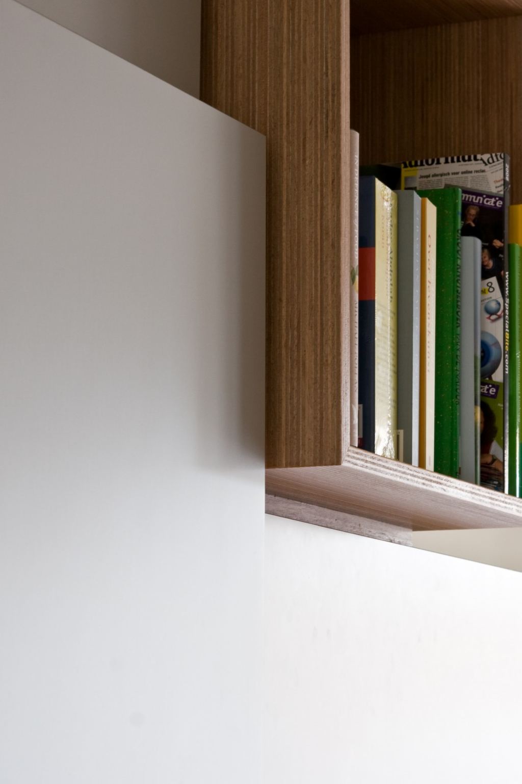 Detail van een open kastvak met tijdschriften, tegen een lichte houten rand.