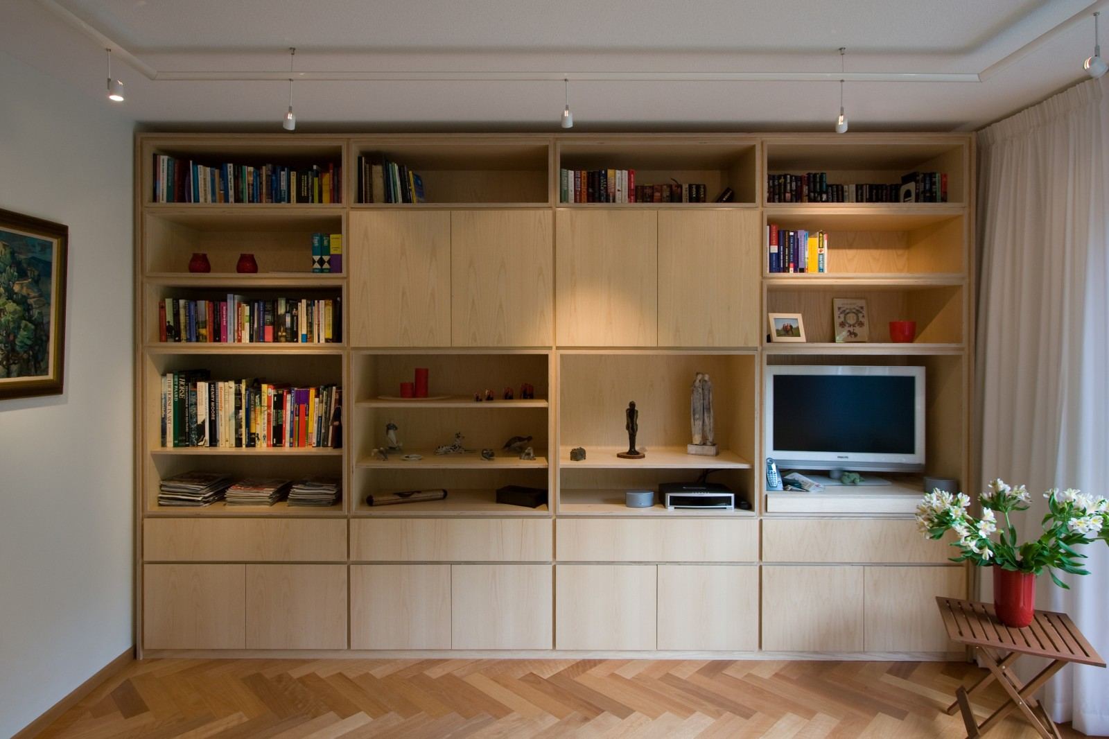 Symmetrische wandkast met vier kolommen open boekenplanken boven gesloten deuren en laden.