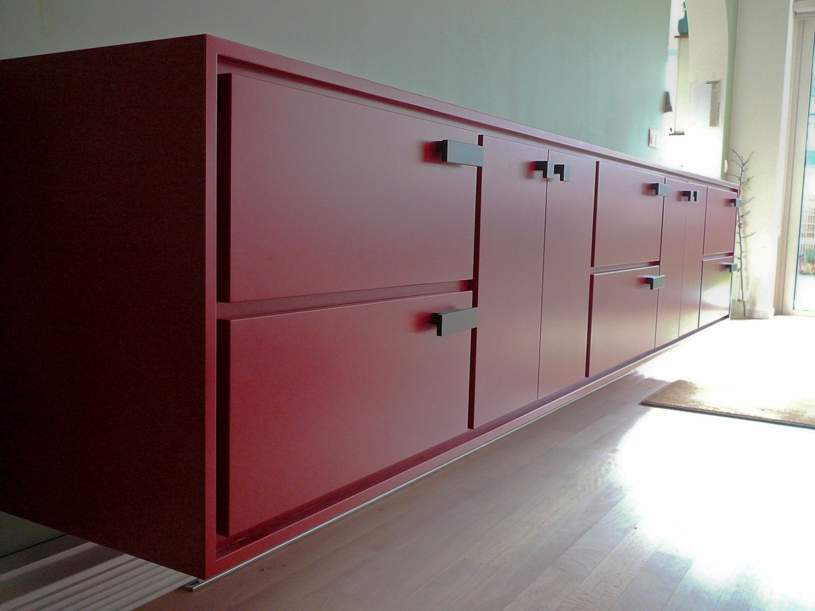 Rood dressoir met opvallende, L-vormige greepjes op de deuren.