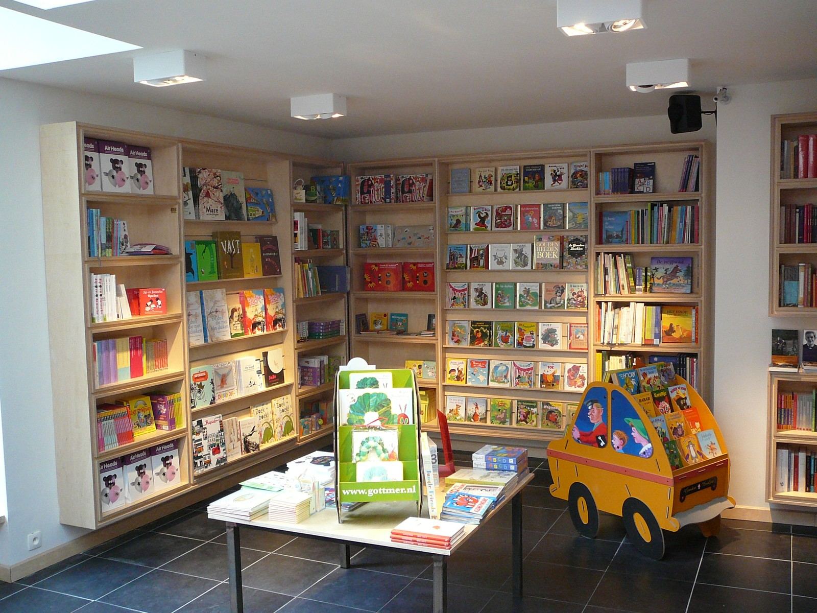 Rek met kleurrijke kinderboeken in vierkante houten vakken.
