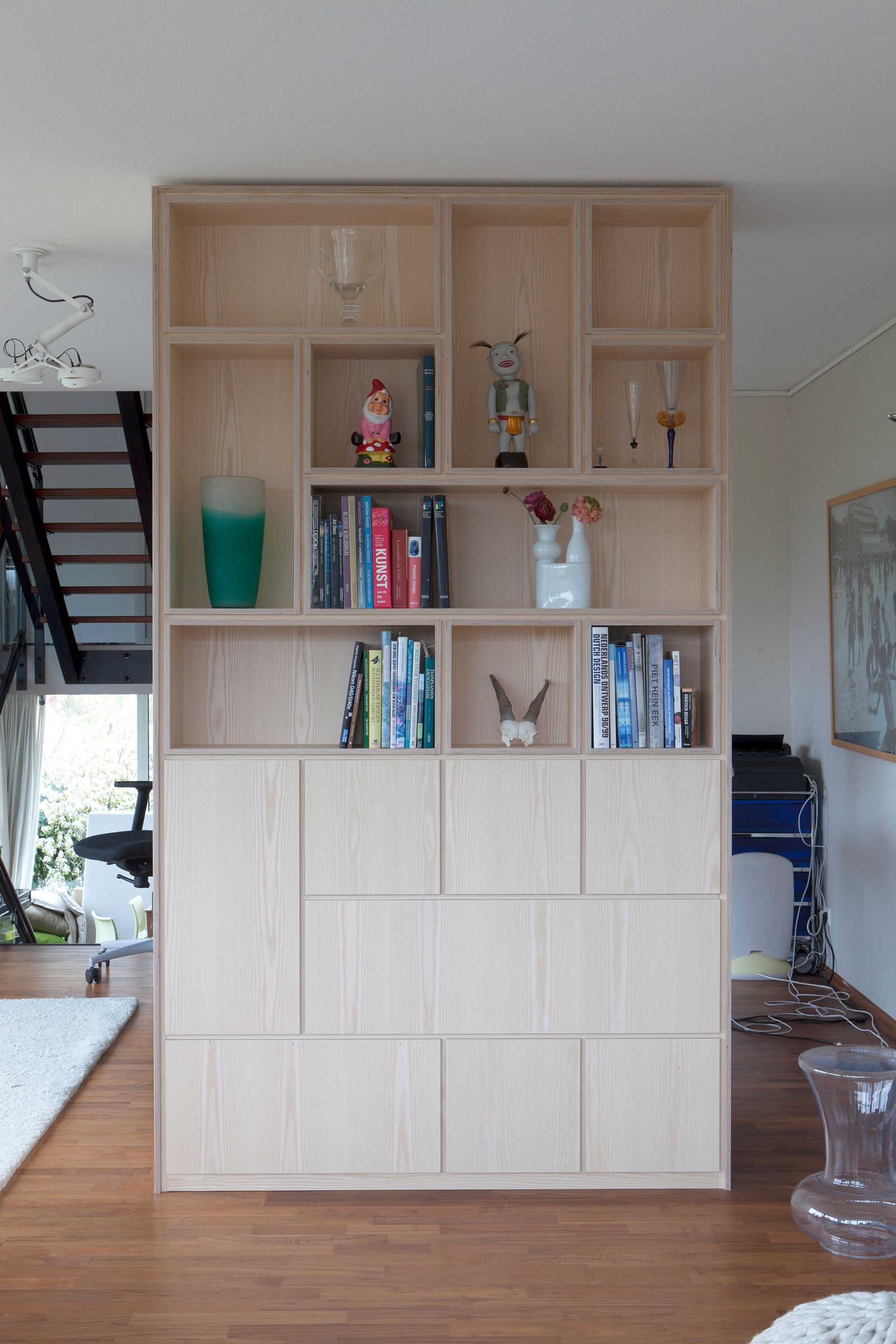 Boekenkast met sculpturale nissen vol beeldjes en boeken, boven gesloten kastdeuren.