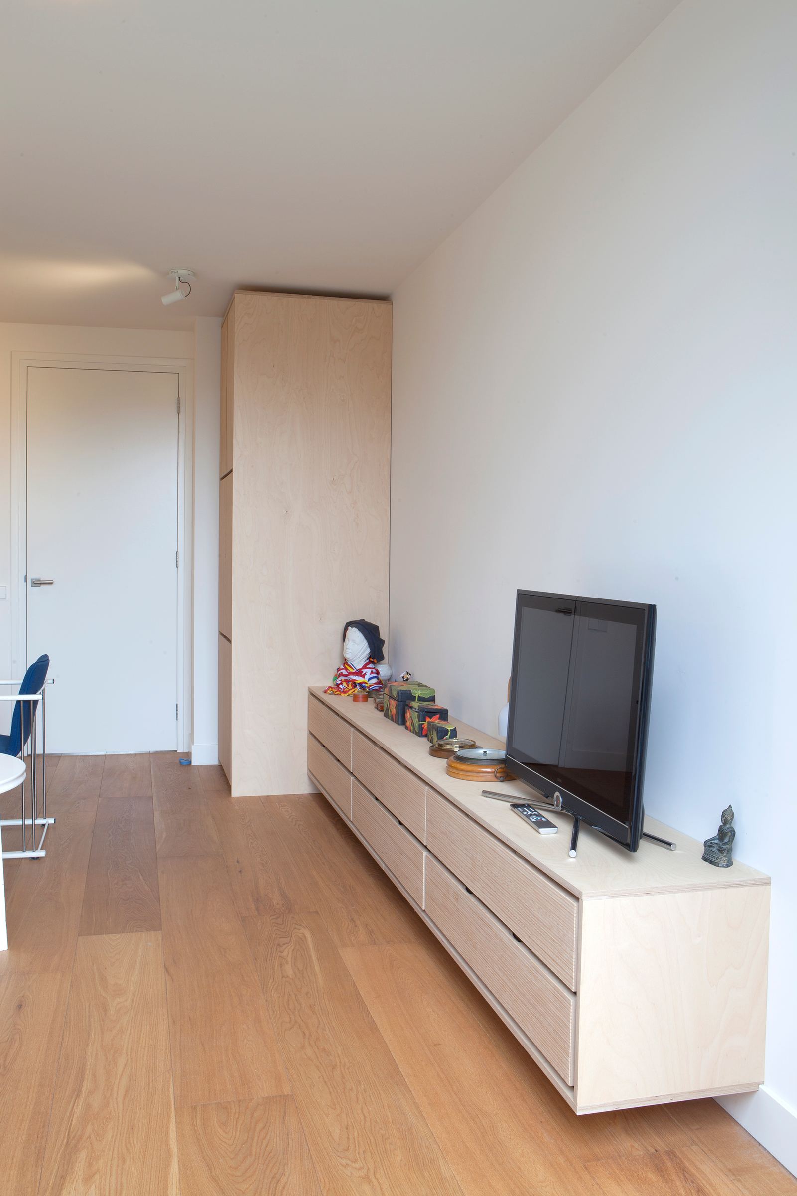 Breed zwevend dressoir van plexwood met televisie en een hoge kastkolom.