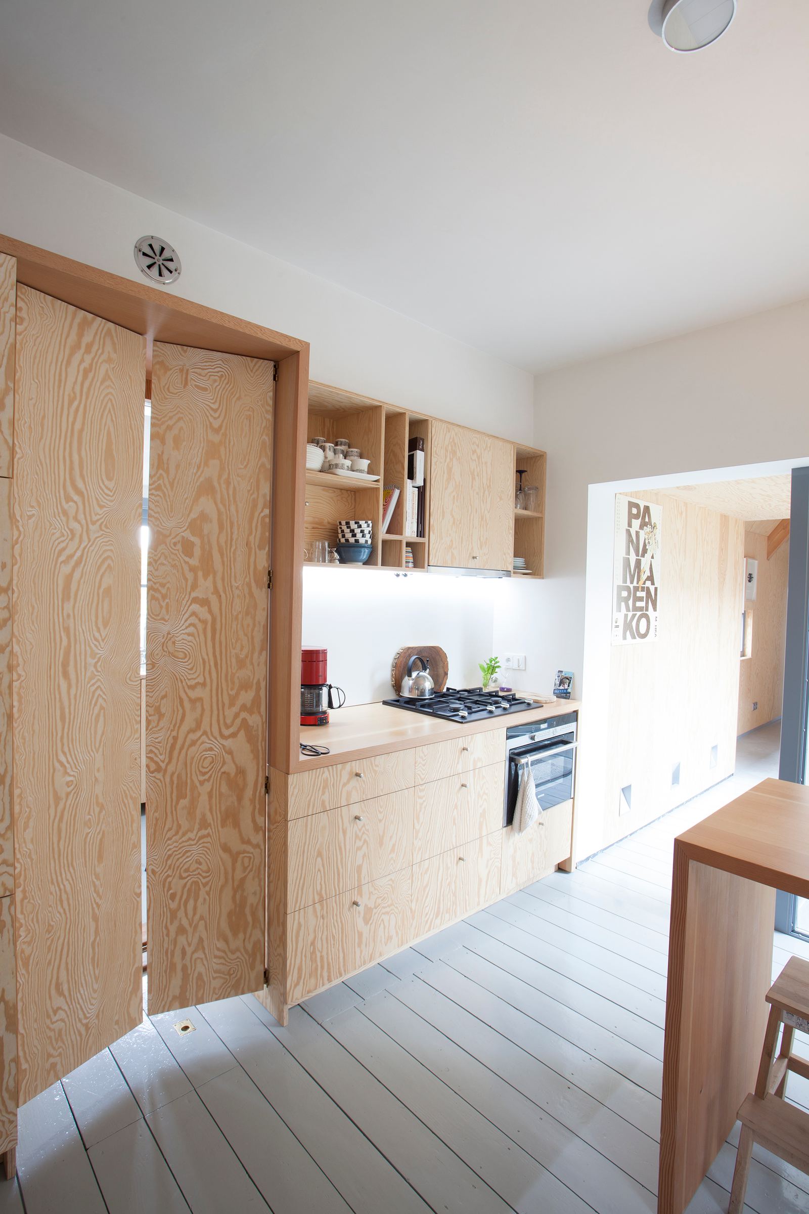 Houten keuken met een openstaande vouwdeur en open wandkasten met servies.