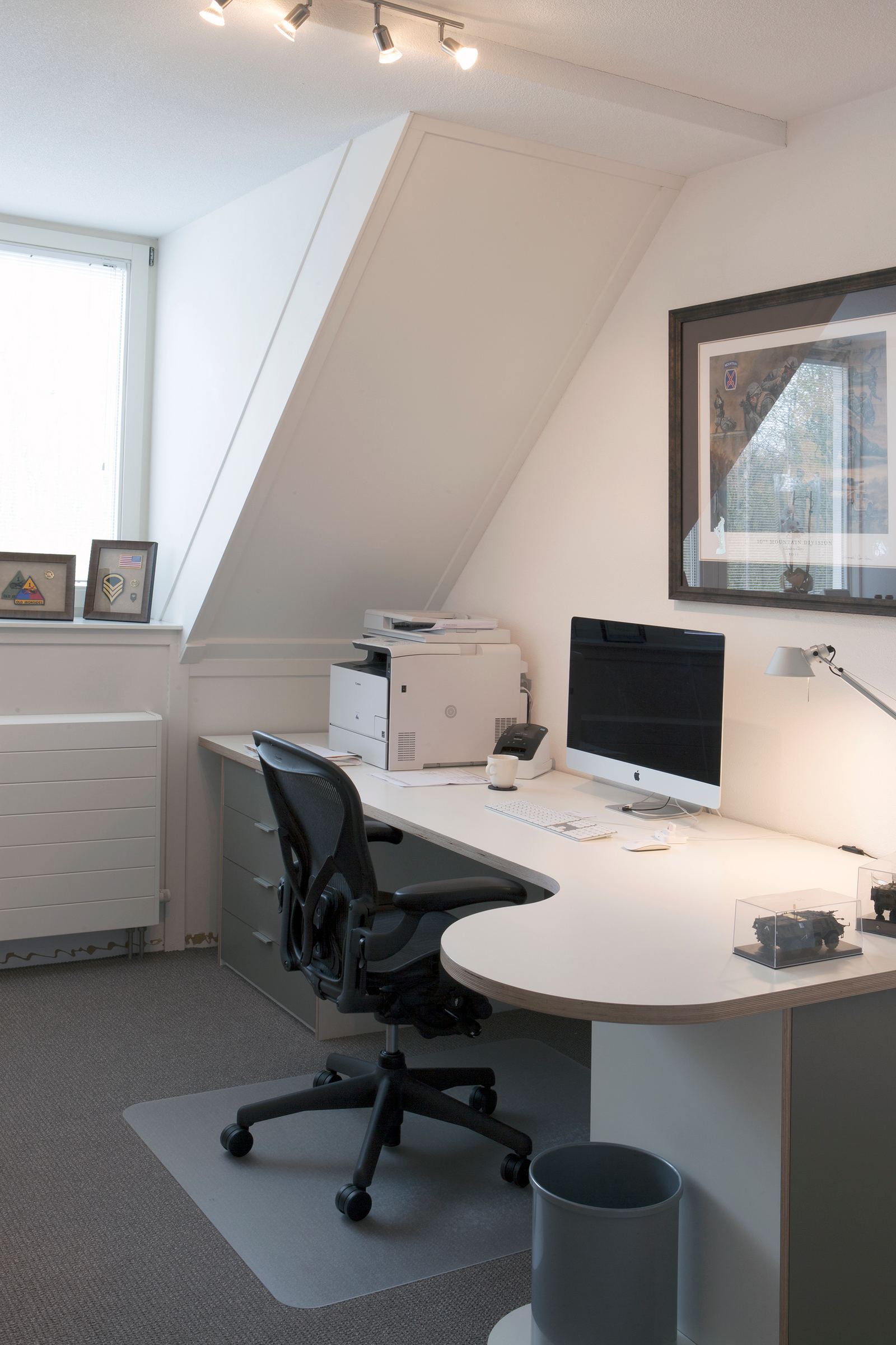 Hoekbureau met een wit blad tegen een schuine zolderwand, met een grijze ladenkast.