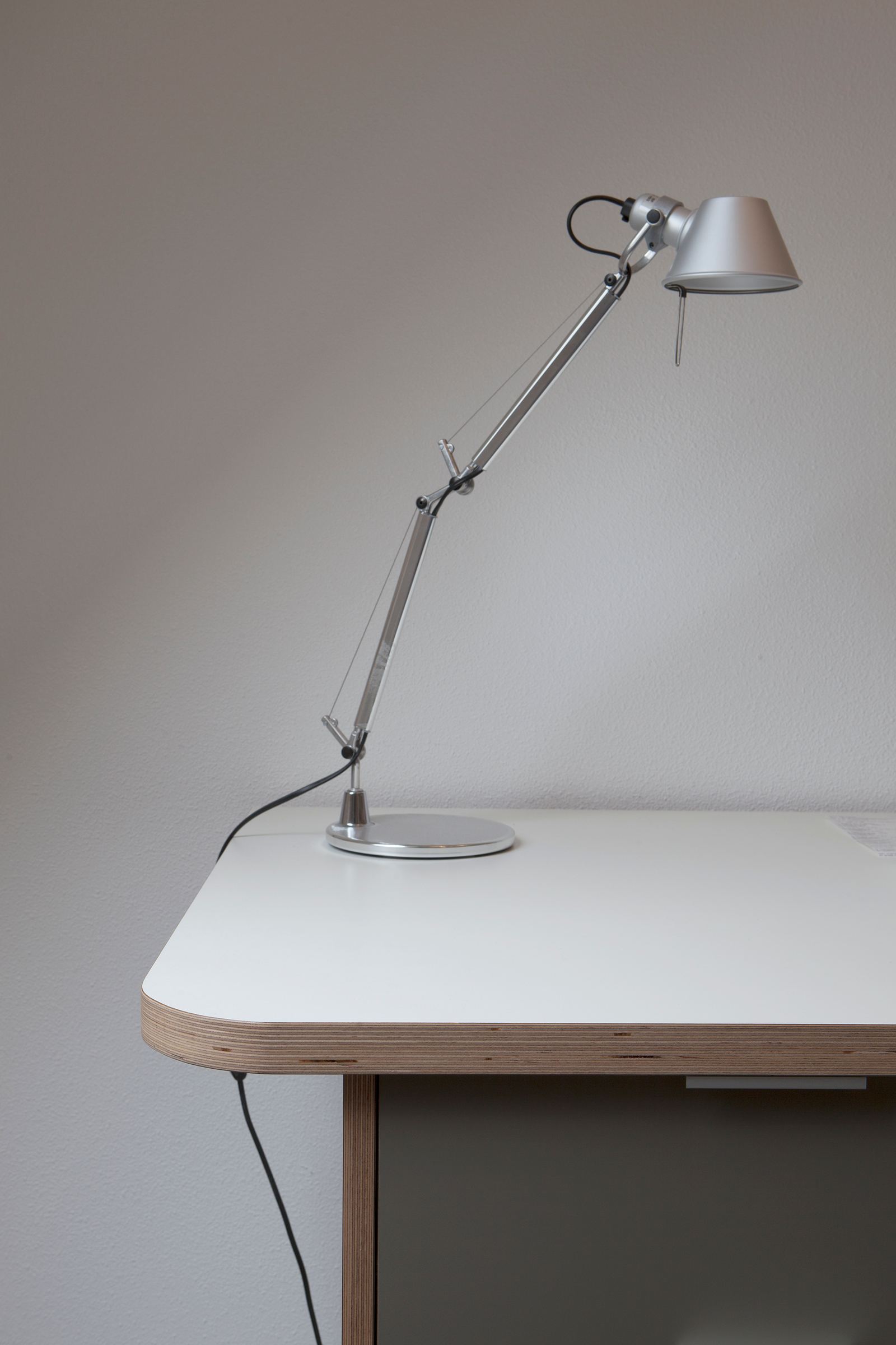 Detail van een wit bureaublad met plaatrand, met een verstelbare bureaulamp erop.