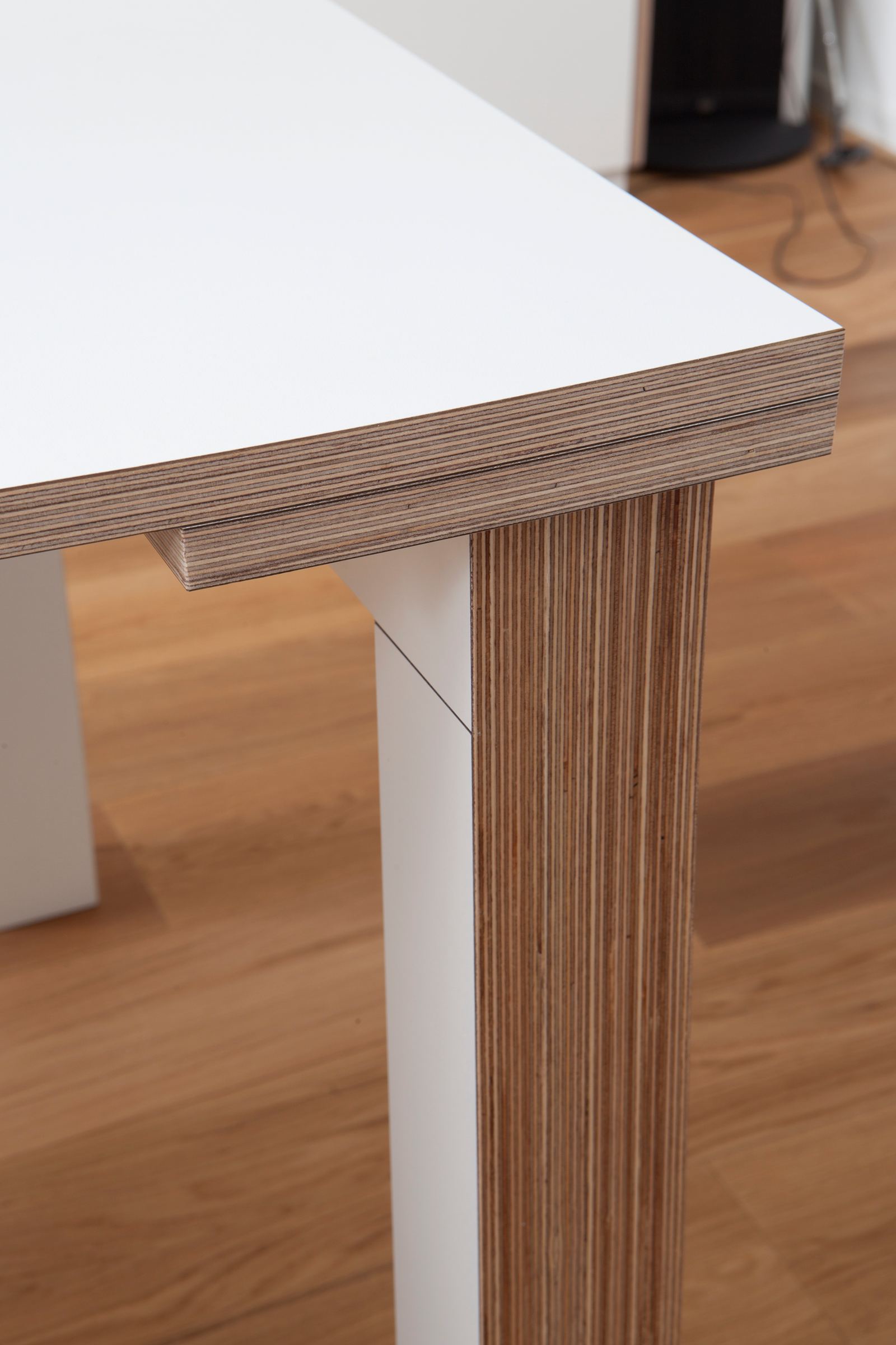 Detail van de hoek van een tafel, met een wit blad op een gestreepte houten poot.