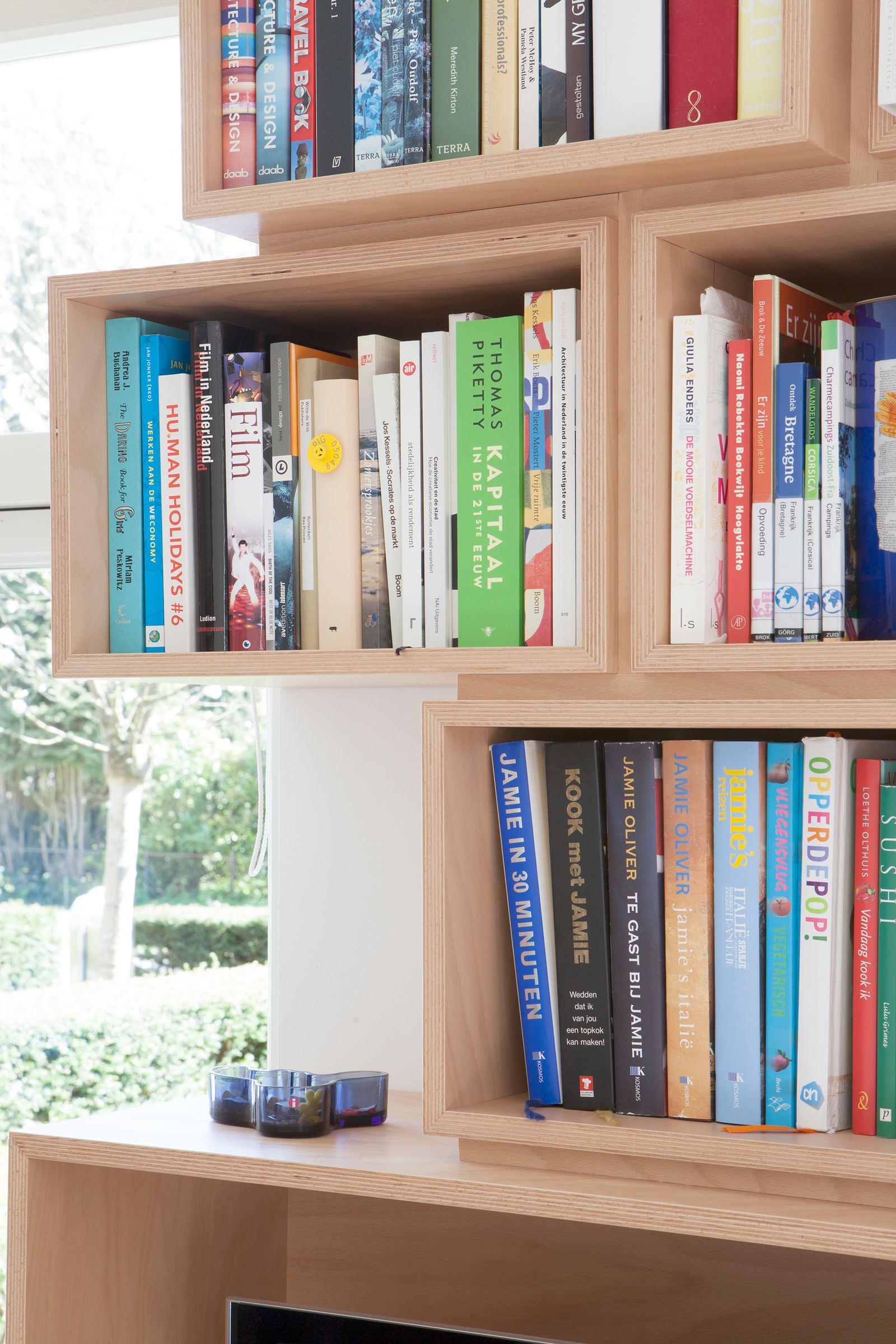 Detail van boeken en een glazen object in een houten kastvak.