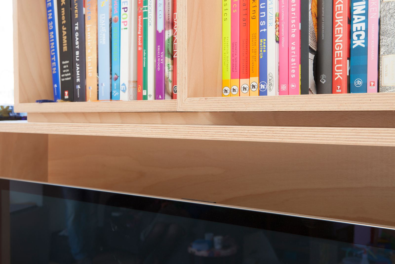 Detail van een rij kookboeken in een houten kastvak.